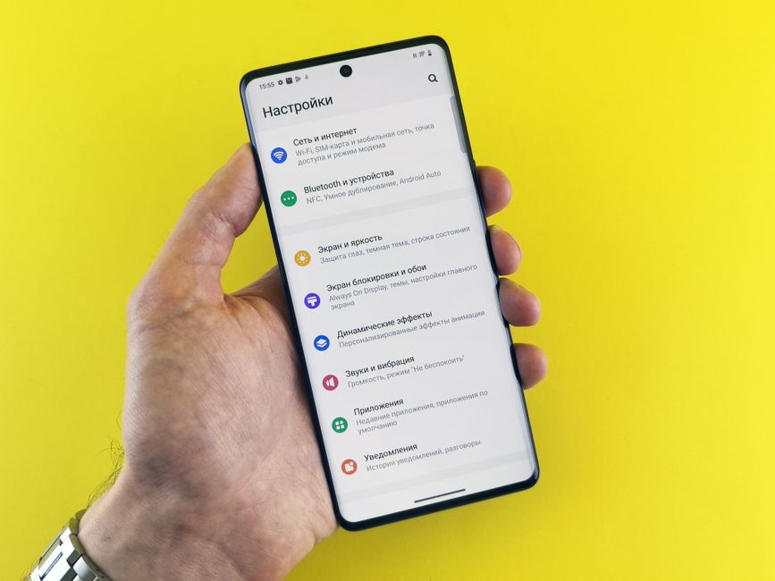 Close-up of a hand holding a smartphone with settings menu on a bright yellow background.