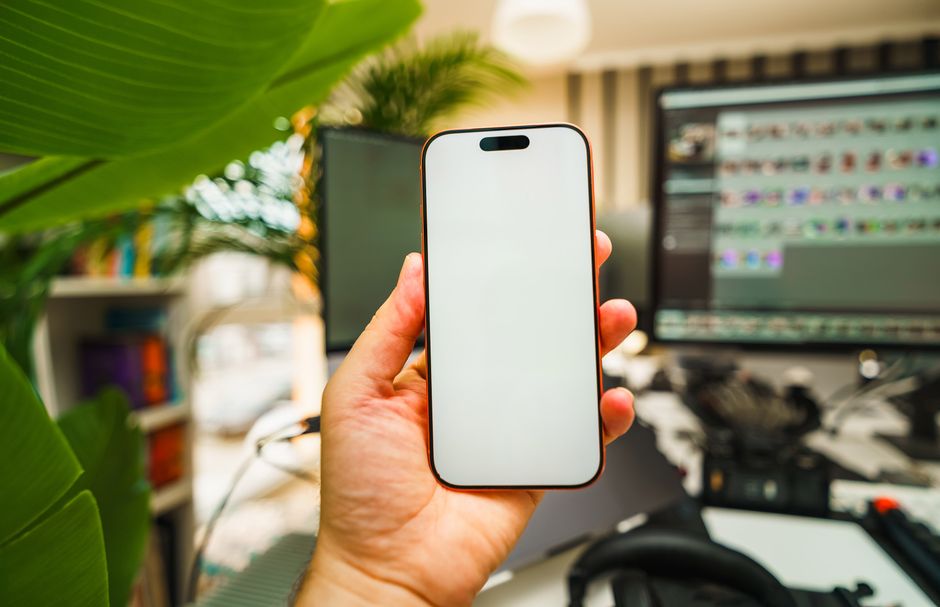 Close-up of a hand holding a smartphone with a blank screen in an office setting.