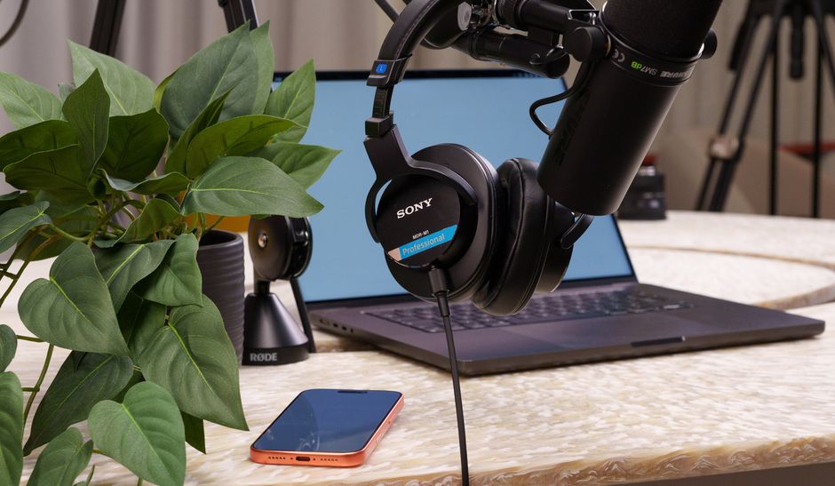 A well-equipped podcast studio featuring a laptop, microphone, headphones, and a smartphone on a stylish desk.