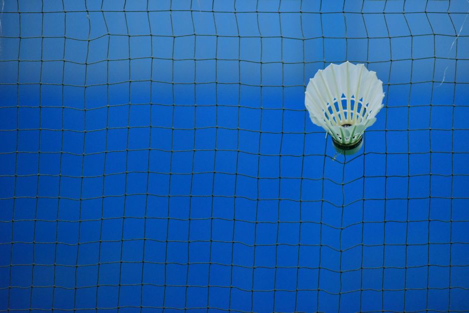Shuttlecock caught in badminton net on blue court, symbolizing sport and challenge.